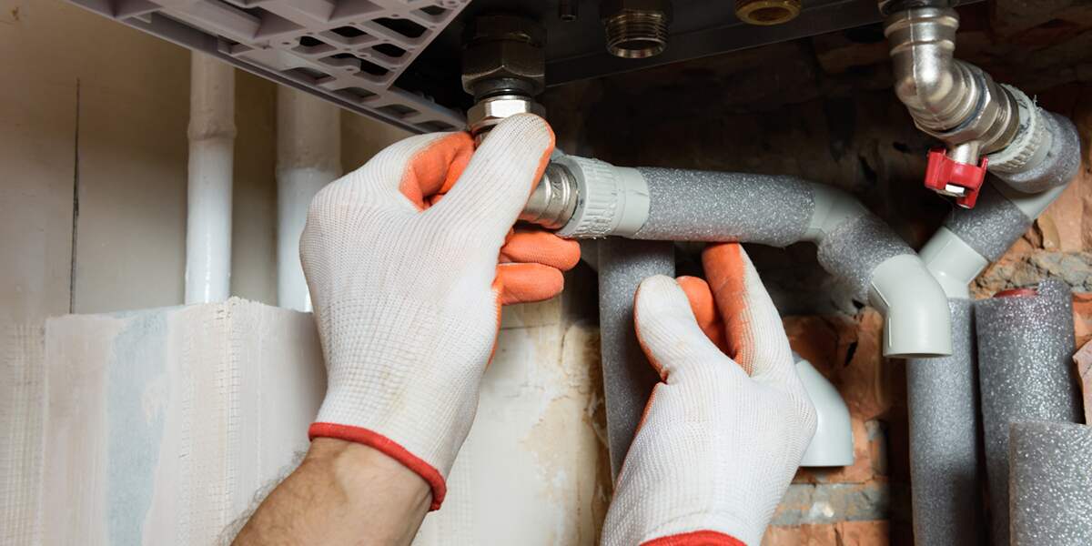 Plumber wearing gloves installing insulated pipes on a heating system