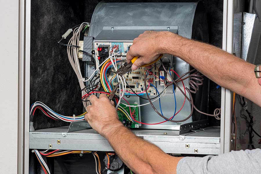 Technician repairing HVAC wiring with pliers inside a furnace unit